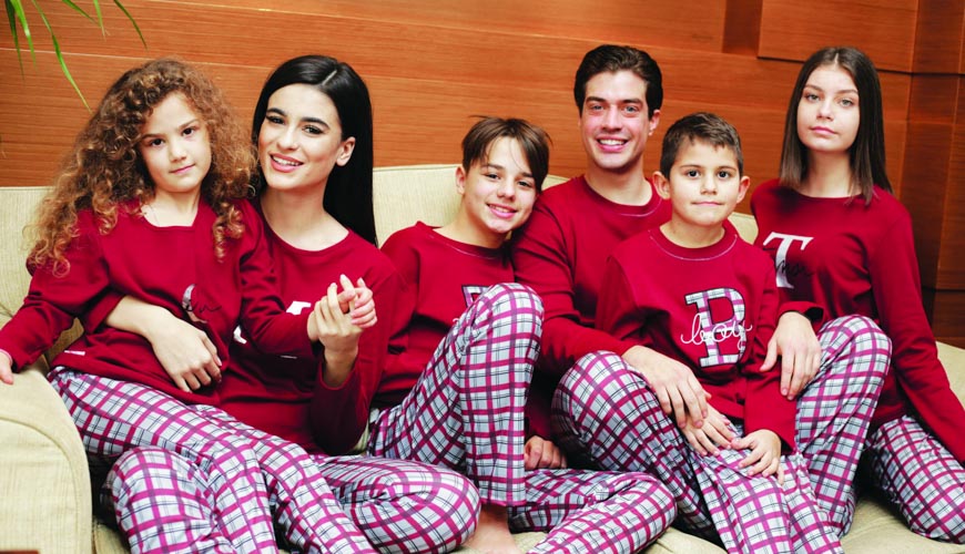 Εξαμελής οικογένεια που φοράει το ίδιο σχέδιο πυτζάμες κάθεται σε μεγάλο καναπέ.