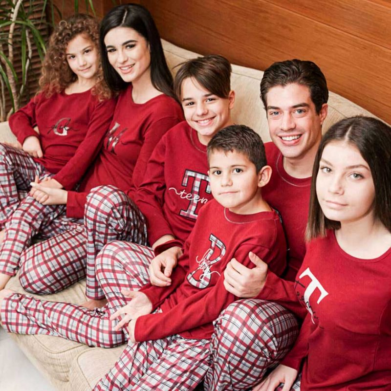Εξαμελής οικογένεια με σετ ταιριαστές πυτζάμες κάθεται σε καναπέ.